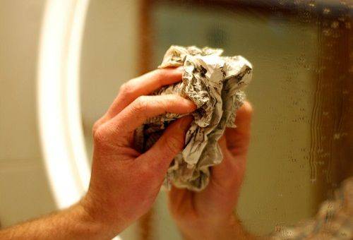woman washes a mirror with a newspaper